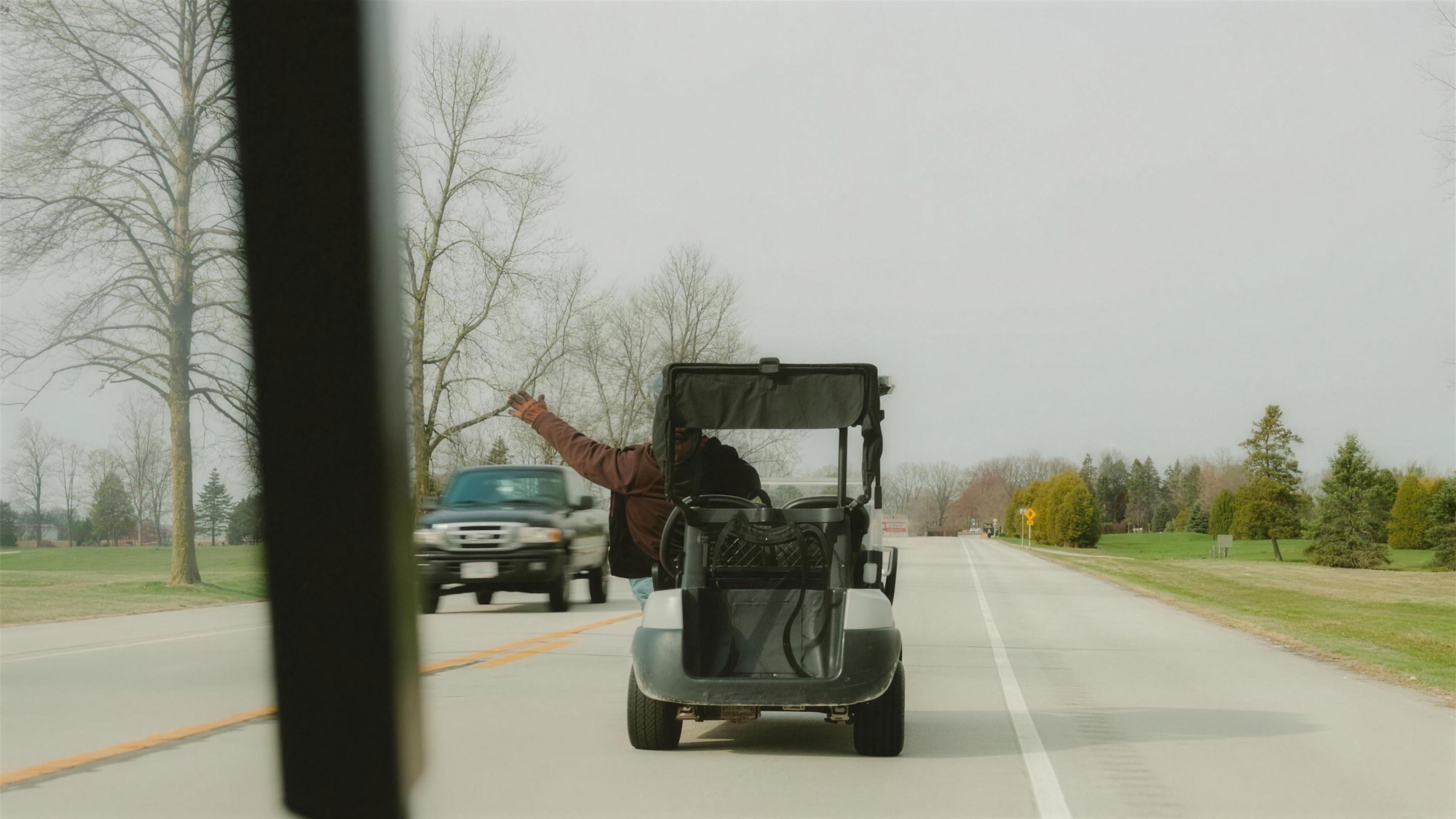 Riding a golf cart down a rural Wisconsin highway, arm raised, pickup truck passing