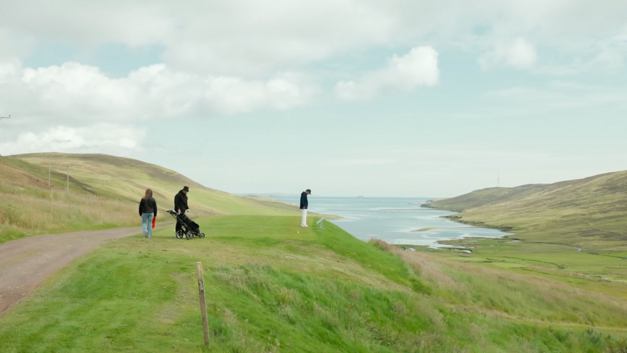 A golfer sets up on a clifftop tee at Whalsay Golf Club, hills and the North Sea stretching out behind him